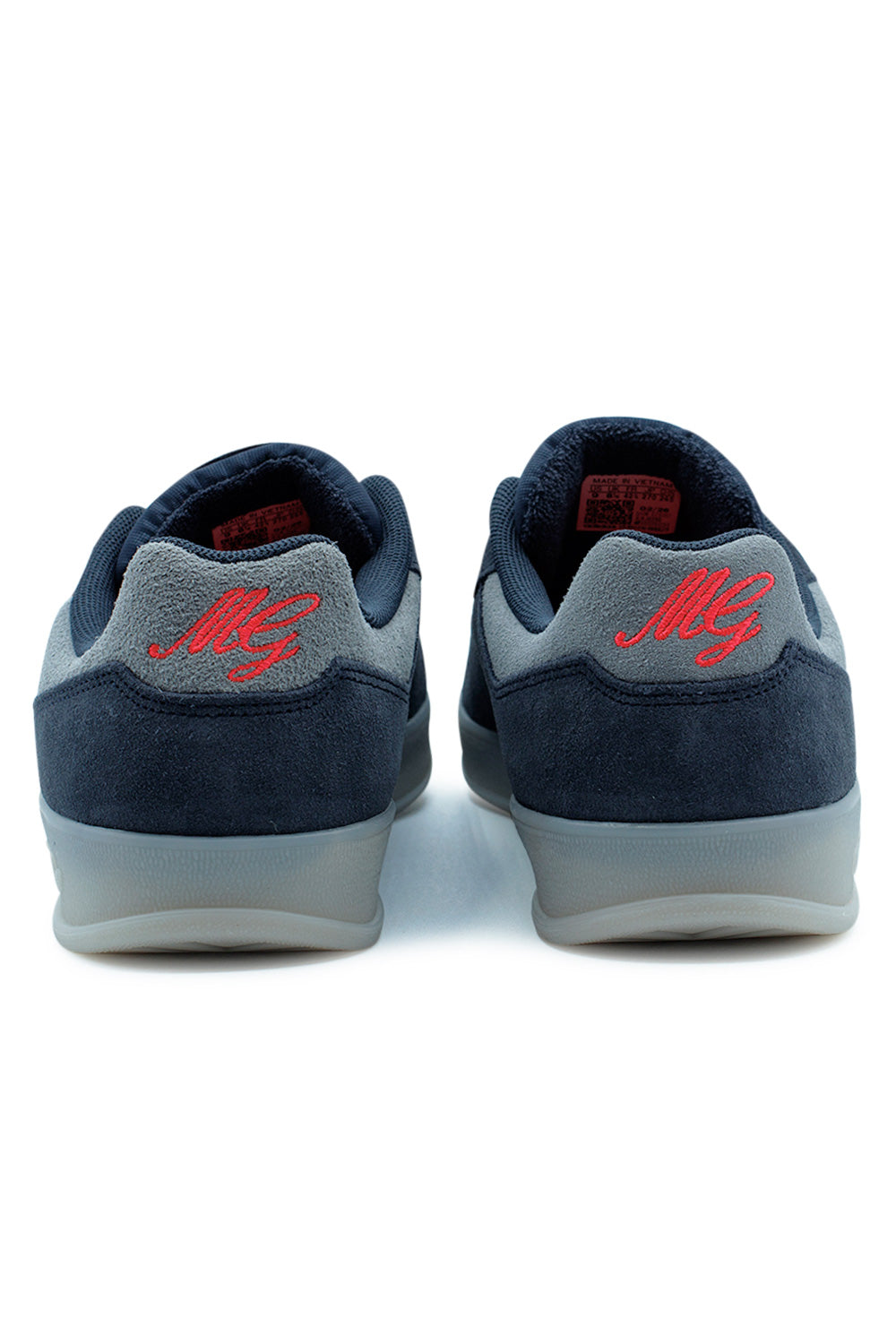 Rear heel view of the adidas Aloha Super shoes, showing the grey suede heel tabs with red embroidered MG Mark Gonzales initials above the translucent sole.