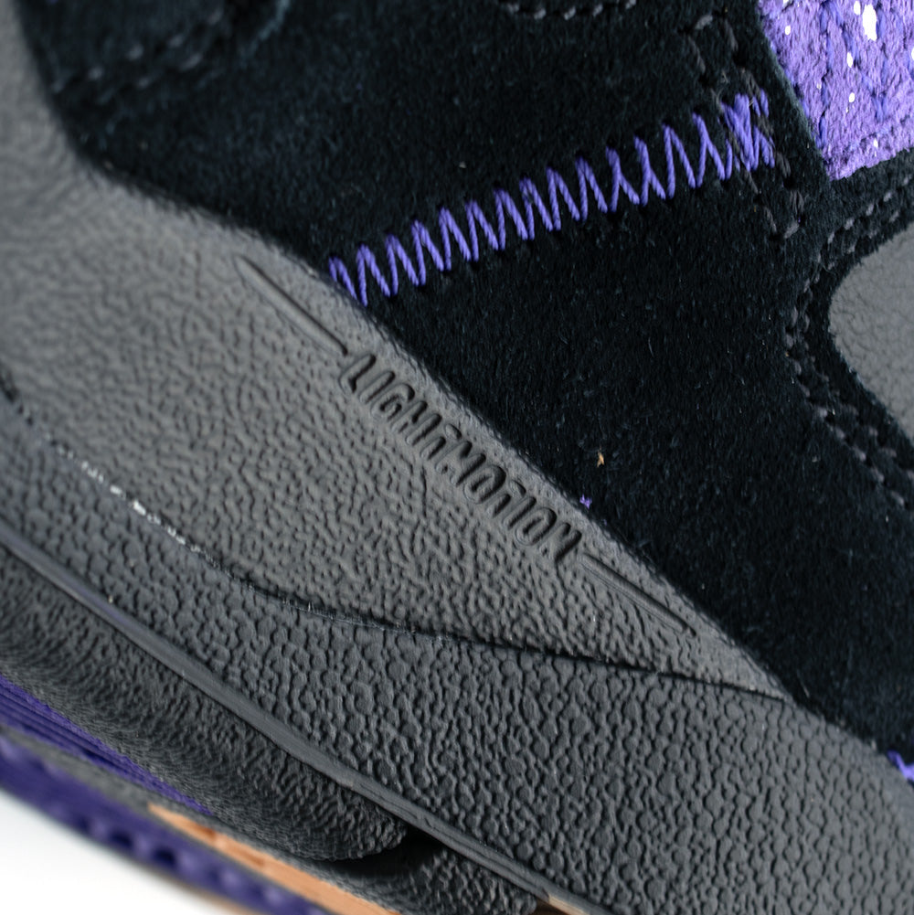 Extreme macro close-up of the black rubber midsole on the adidas Kader, highlighting the textured sidewall molding debossed with technical "LIGHTMOTION" cushioning branding, accented by heavy purple reinforcement stitching above the sole line.