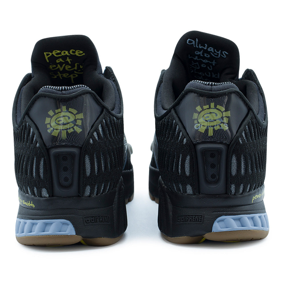 Rear studio perspective of the adidas x Always Do What You Should Do Climacool 1 heels, displaying the lenticular badges that shift between the green ADWYSD @Sun logo and the adidas badge of sport, molded heel ventilation ducts, inner tongue handwritten embroidery reading "peace at every step" and the brand name, and segmented adiPRENE midsoles.