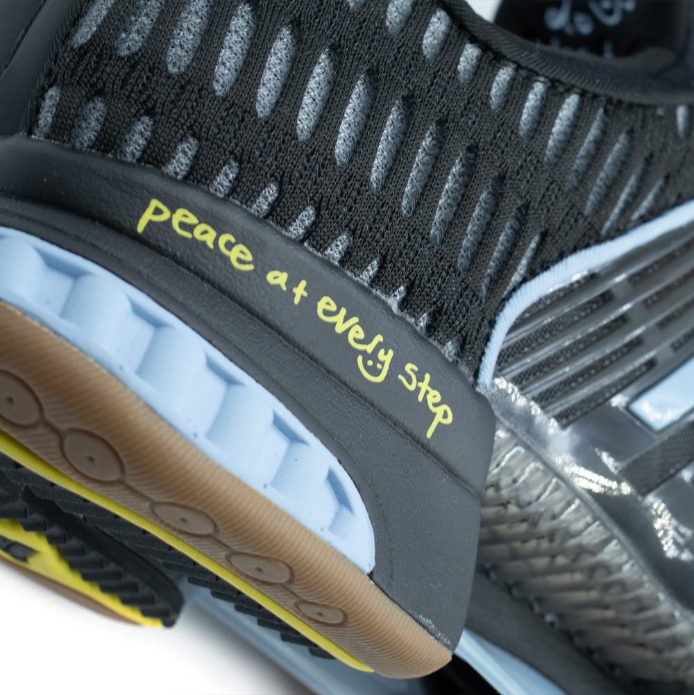 Macro perspective of the lateral rear heel on the adidas x ADWYSD Climacool 1, capturing the pale yellow script reading "peace at every step" stamped on the black heel counter, segmented light blue foam heel crash pad, and the ribbed mesh upper.