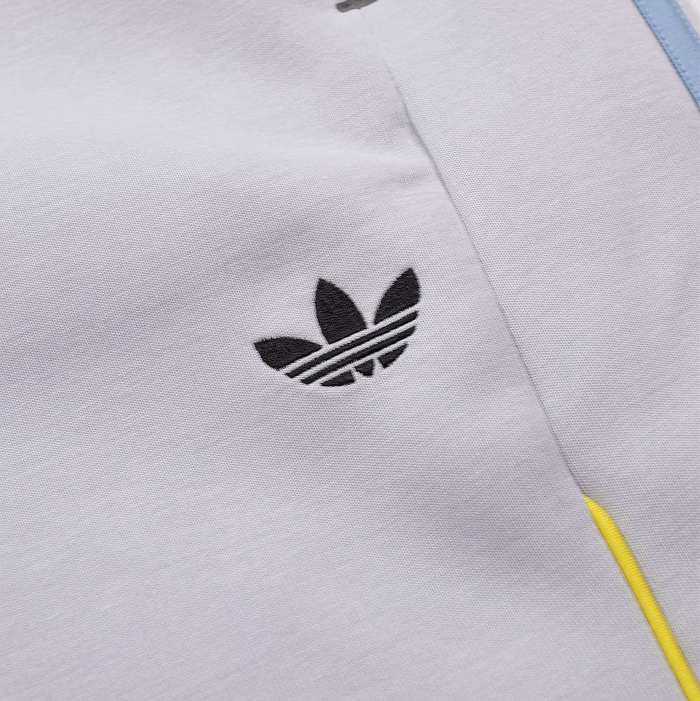 Detailed macro close-up of the front thigh on the adidas x ADWYSD Pant, capturing the clean black embroidered classic adidas Trefoil brand logo positioned above the curved neon yellow piping accent on light solid grey fabric.