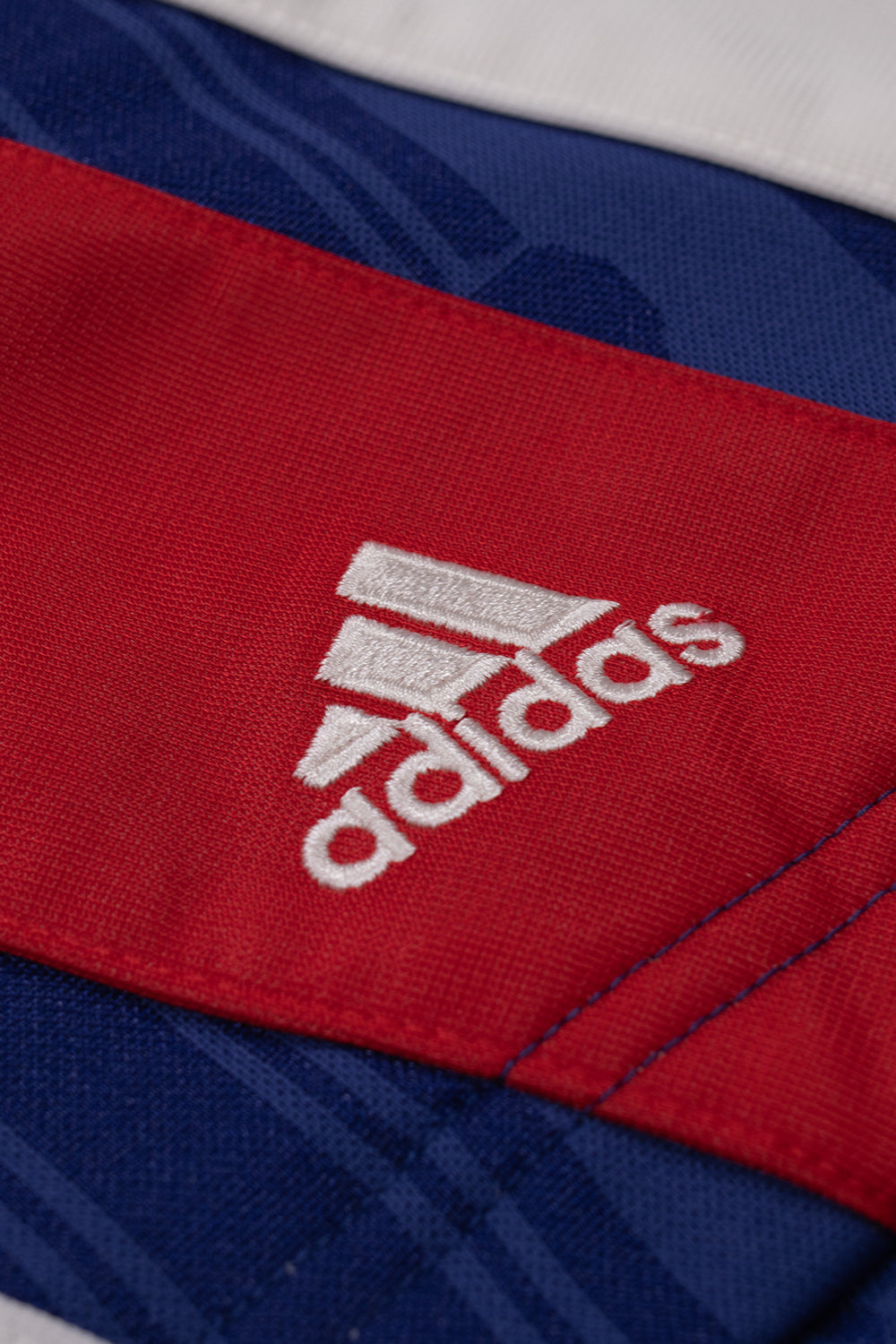 Close-up of the embroidered adidas logo on the adidas x Brain Dead x Disney Football Short Victory Blue showcasing premium embroidery, sewn-on three stripe panels and vintage football styling