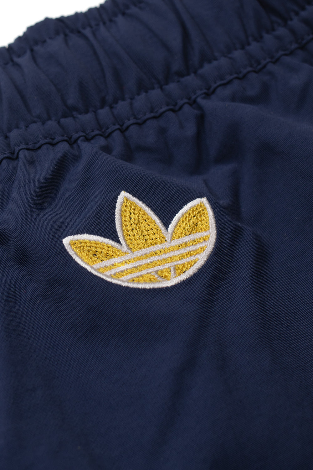 Close-up of the embroidered gold adidas Trefoil logo on the back of the adidas x Brain Dead x Disney Short Core Navy featuring premium craftsmanship, lightweight fabric and exclusive World Cup capsule branding
