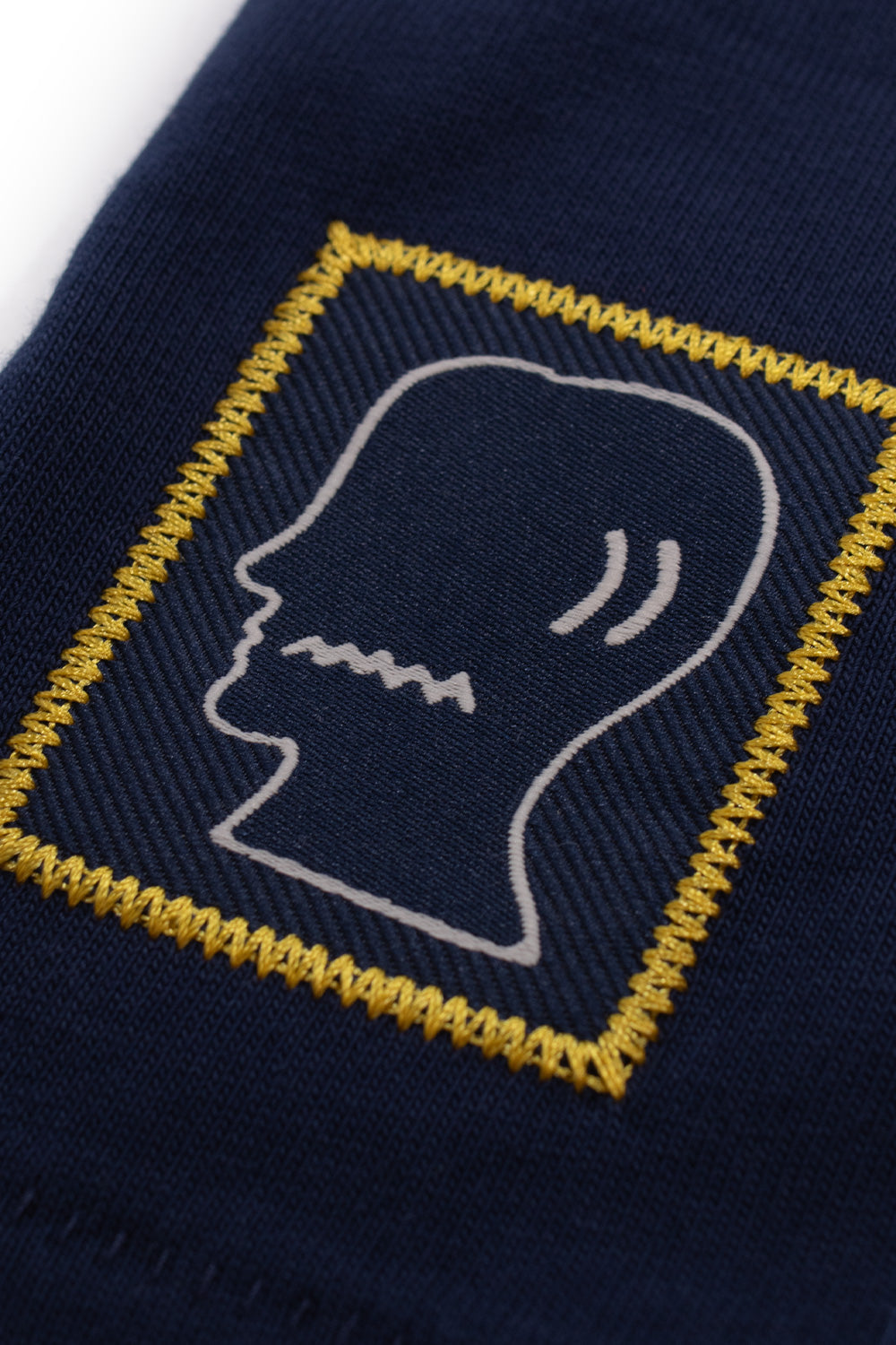 Macro shot of the sewn Brain Dead logo patch on the Adidas Originals x Brain Dead x Disney T-Shirt Core Navy, highlighting embroidered detailing, premium craftsmanship, limited capsule collection branding and heavyweight cotton quality.