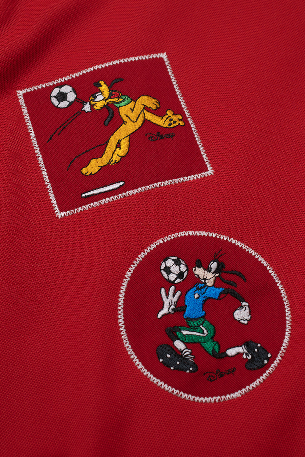 Detailed embroidery of Pluto and Goofy football graphics on the Adidas x Brain Dead x Disney Track Top Better Scarlet, highlighting premium stitched Disney artwork, World Cup capsule collection patches and textured retro sportswear fabric.