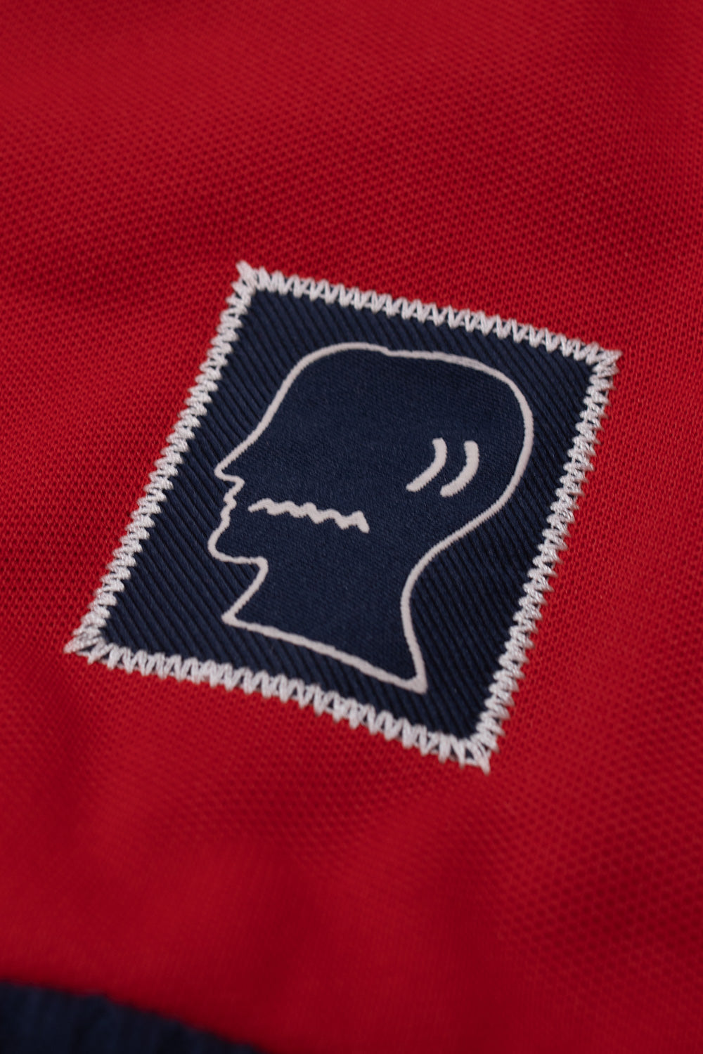 Macro view of the signature Brain Dead woven patch on the Adidas x Brain Dead x Disney Track Top Better Scarlet, displaying premium embroidery, collaborative branding, heavyweight fabric texture and limited edition sportswear finish.