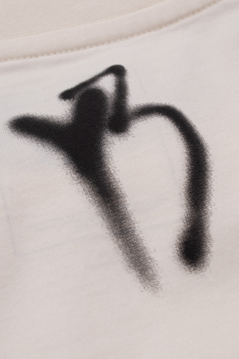 Detailed view of the black airbrushed spray paint Yohji signature tag graphic printed below the ribbed neckline on the back of the chalk white Adidas Y-3 x Chito Graphic Tee.