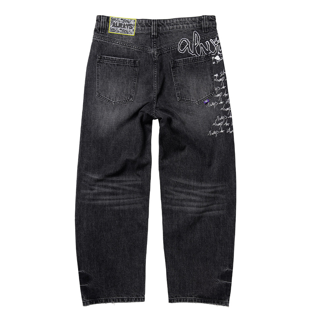 Back flat lay view of the Always Do What You Should Do Waza Jeans in washed black denim, featuring a yellow-framed textured black jacron patch on the waistband, dual rear patch pockets, washed-out whiskering behind the knees, a purple woven tag, and a white screen-printed graffiti tag wrapping from the right hip around to the side seam.