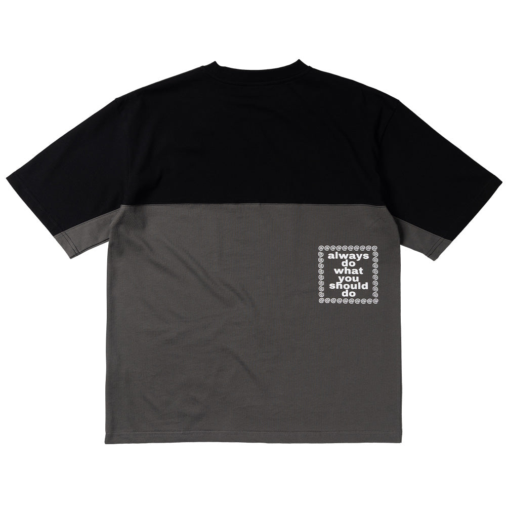 Back flat lay view of the Always Waza Panelled T-Shirt, displaying the horizontal color-blocked cut-and-sew paneling in solid black and charcoal grey heavy cotton, dropped shoulder seams, and a square screen print on the lower right flank reading "always do what you should do" framed by repeated white "@" symbols.
