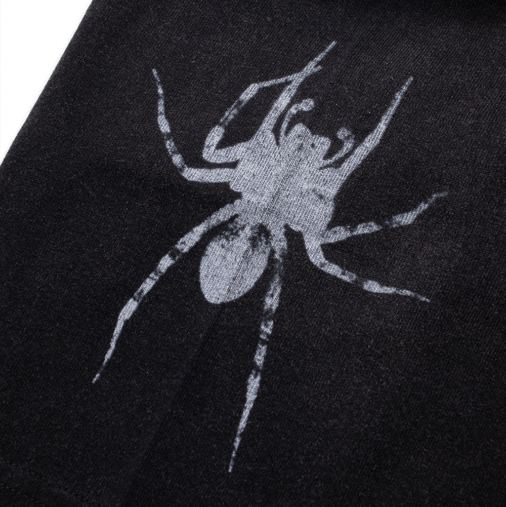 Detailed macro view of the sleeve print on the Born X Raised Llorona T-Shirt, highlighting the high-contrast grey-and-white ink illustration of a detailed garden spider with outstretched spiny legs printed vertically along the sleeve seam.