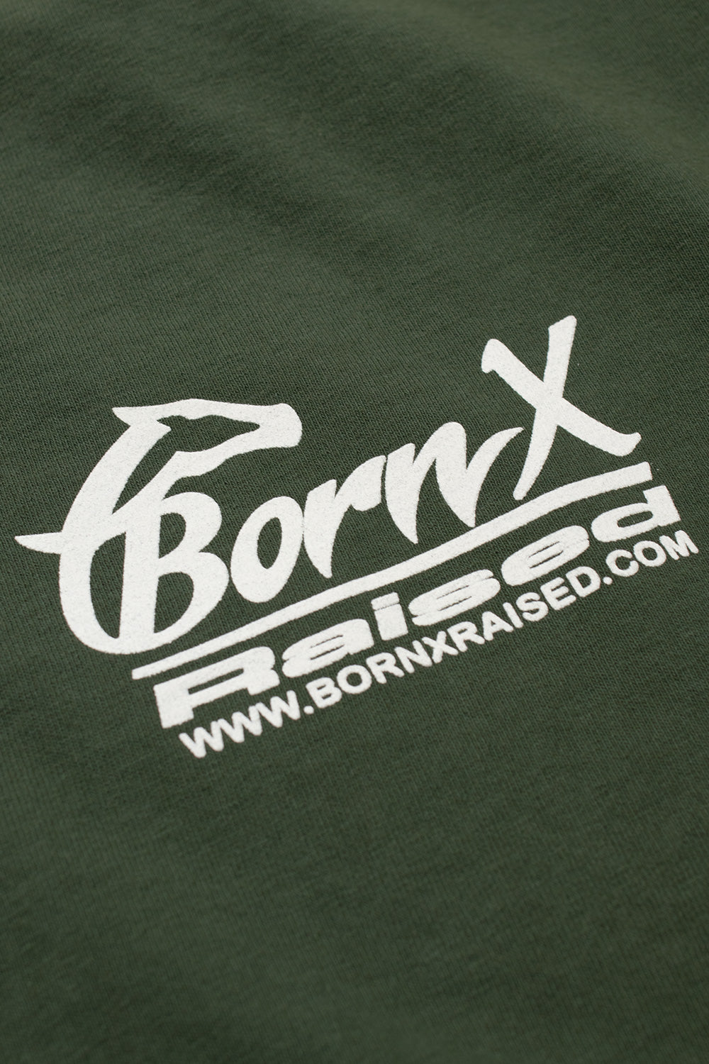 Close-up detail of the white printed Born X Raised horse head graphic and website URL on the soft army green cotton fabric.