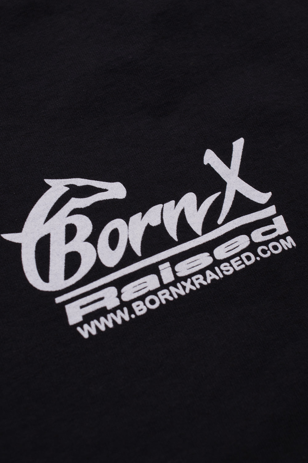 Close-up detail of the white printed Born X Raised horse head graphic and website URL on the soft black cotton fabric.