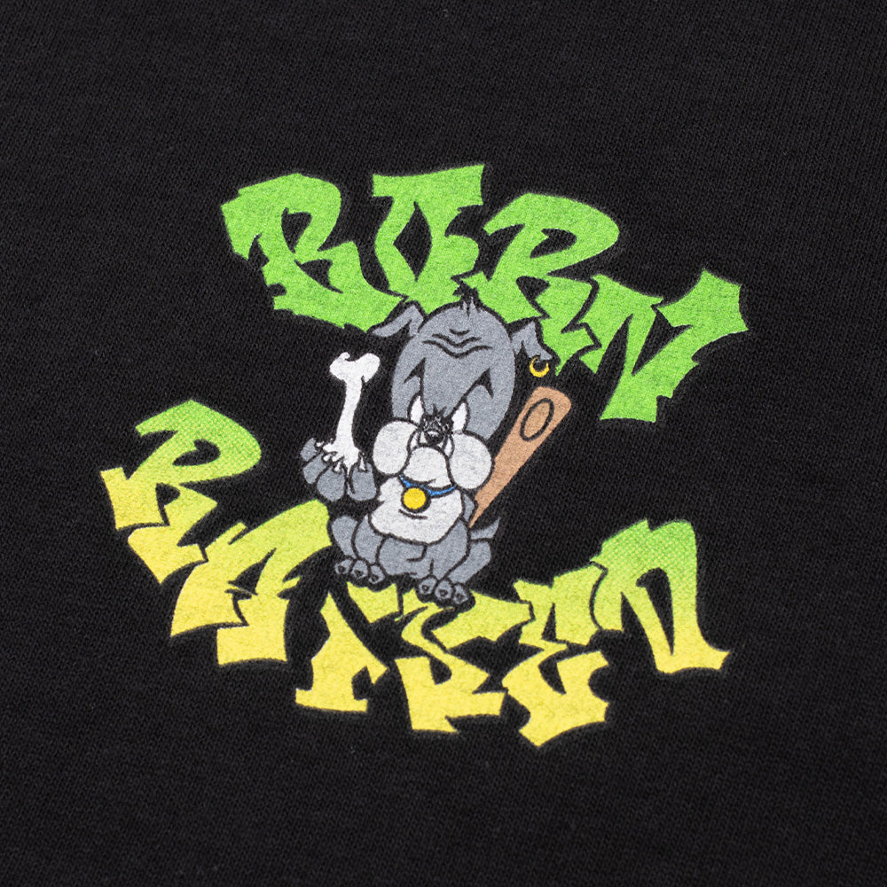 Detailed macro perspective of the screen-printed artwork on the Born X Raised Puppy T-Shirt, highlighting the textured print of the grumpy bulldog puppy with a gold earring, blue collar, chew bone, and wooden bat, set between lime-green and bright yellow shaded graffiti block text on black cotton jersey.