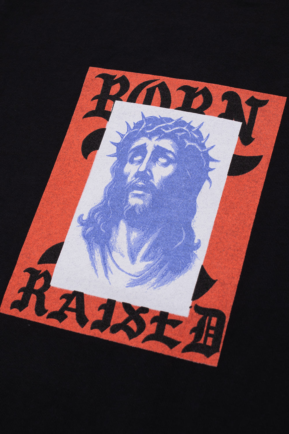 Close-up detail of the chest graphic showing a blue Jesus with a crown of thorns portrait layered over a red background with Old English Born X Raised lettering.