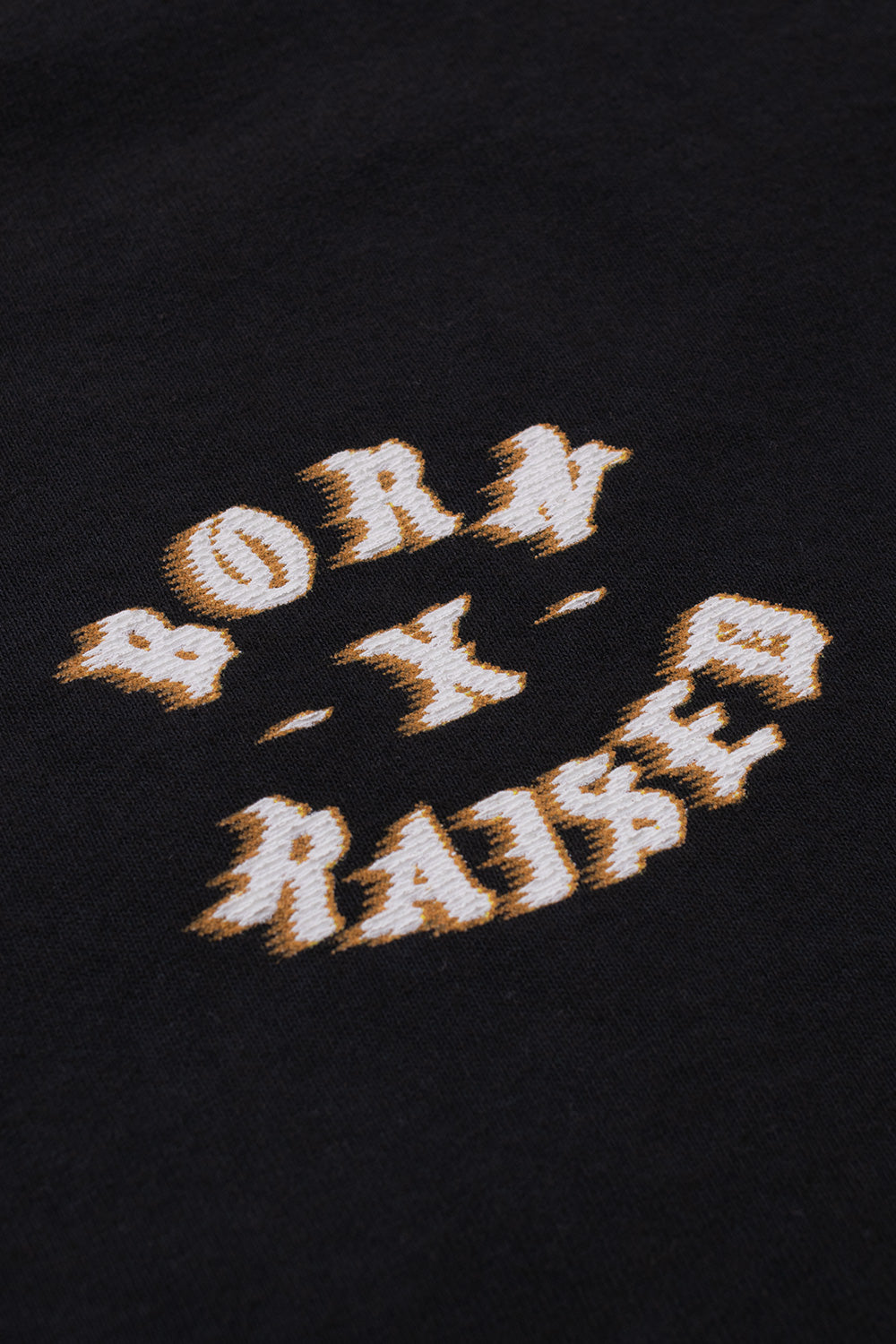 Close-up detail of the yellow and white speed-blur effect printed Born X Raised logo graphic on the soft black cotton fabric.