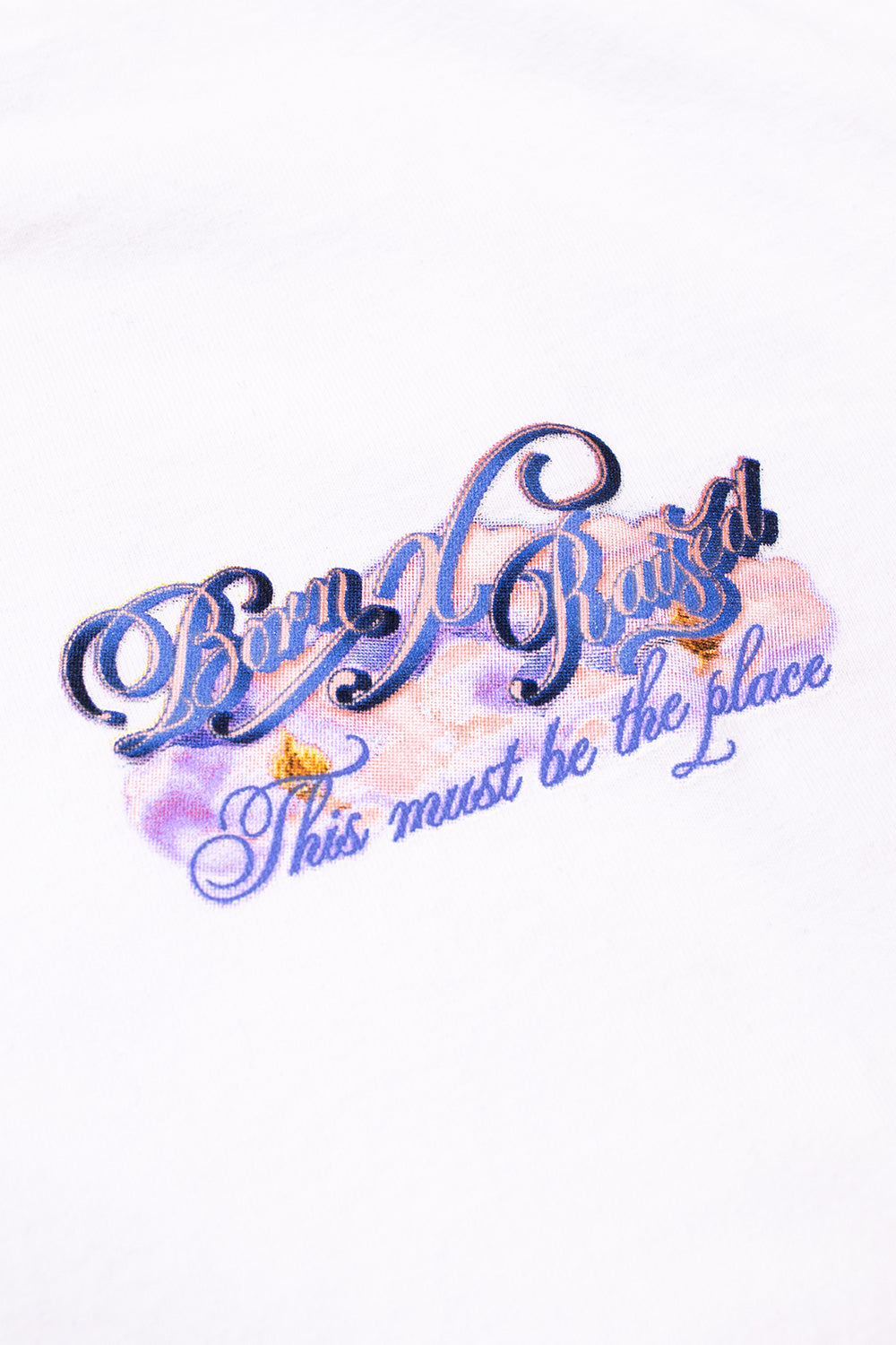 Detailed view of the chest print featuring the script Born X Raised logo and This must be the place slogan over a purple cloud background.