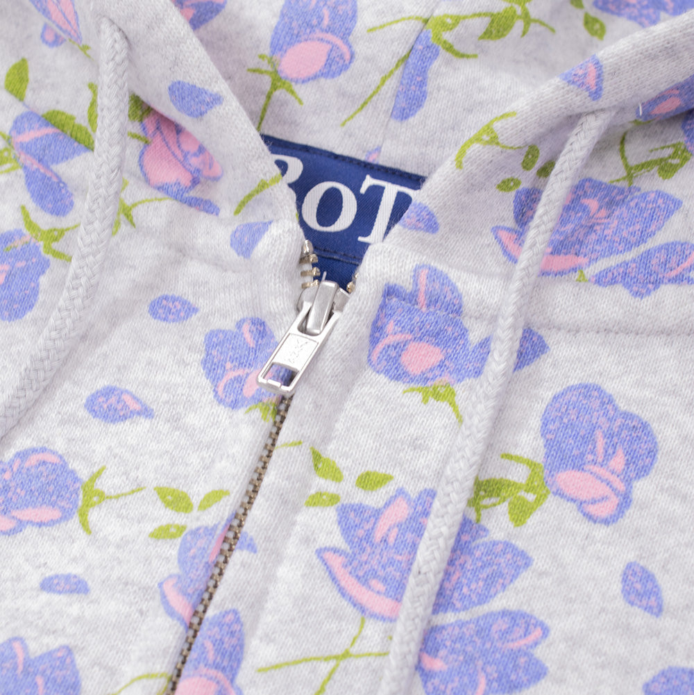 Macro studio close-up of the neckline and hood on the BoTT Flower Zip Hoodie Ash, detailing the polished silver metal YKK zipper puller, round braided grey drawcords, woven blue "BoTT" brand neck label, and the soft texture of the floral printed ash fleece fabric.