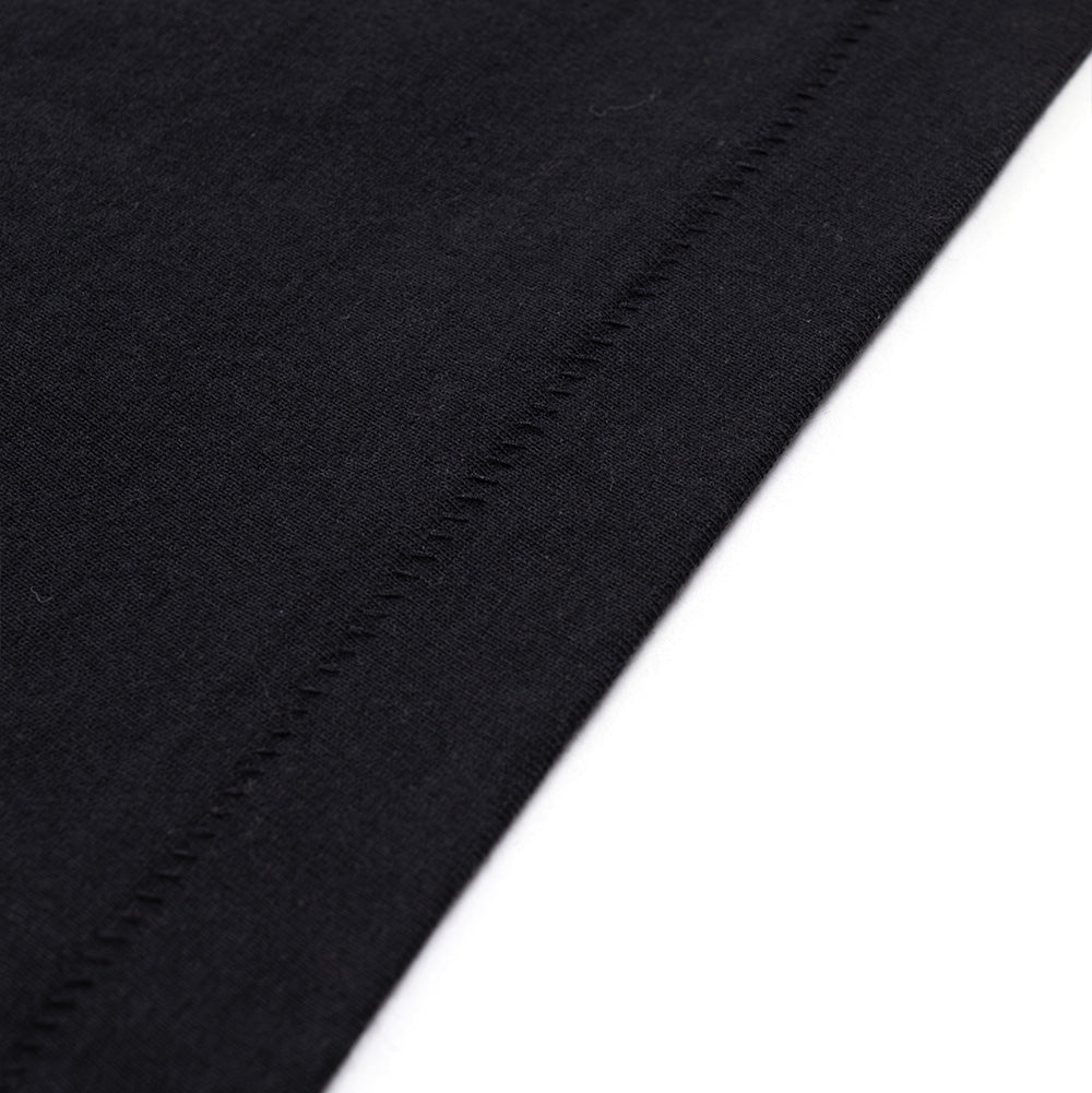 Macro studio view of the bottom hem on the BoTT Shaved T-Shirt in Black, focusing on the clean blind-stitch hemline, dense weave, and smooth matte finish of the premium heavyweight cotton jersey textile.