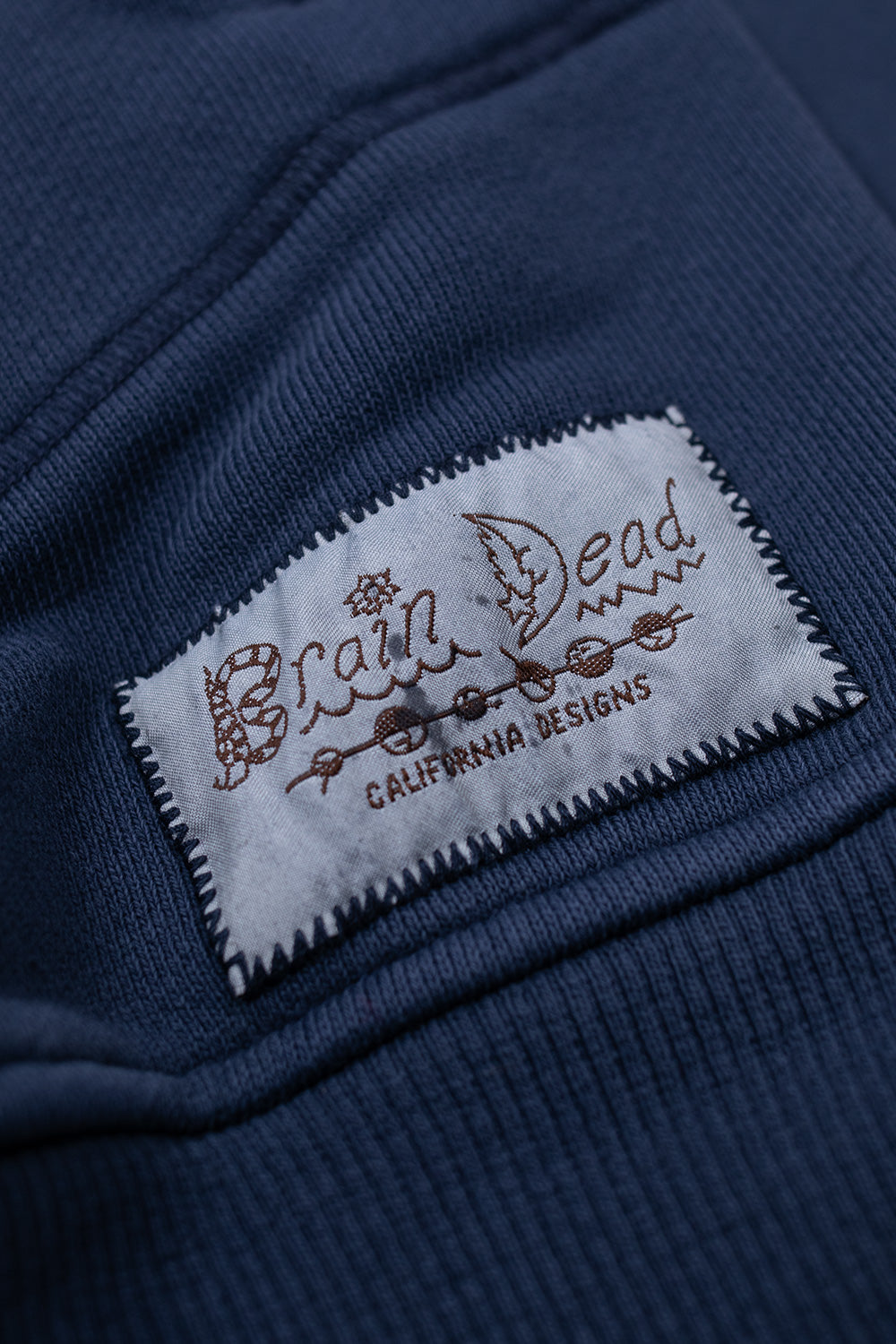 Brain Dead California Designs stitched logo patch on Midnight Half Zip Collared Sweatshirt showcasing branded label detail on premium cotton streetwear pullover
