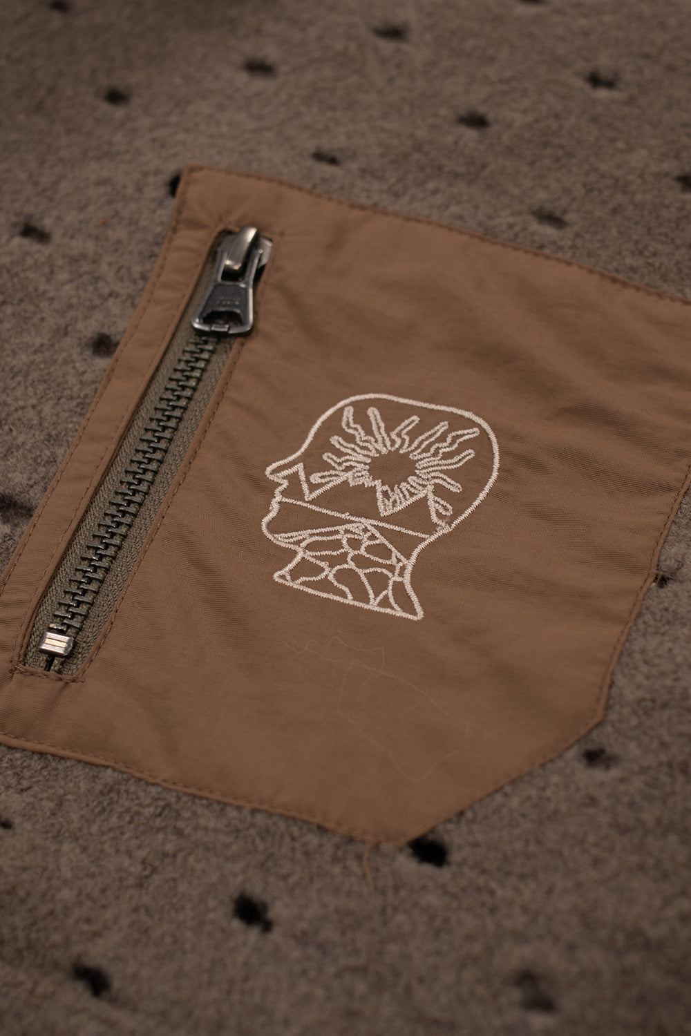 Close-up of the Brain Dead Hole Mock Neck Pullover Brown chest pocket featuring YKK zipper, embroidered Brain Dead logo, nylon contrast panel and premium outdoor-inspired details