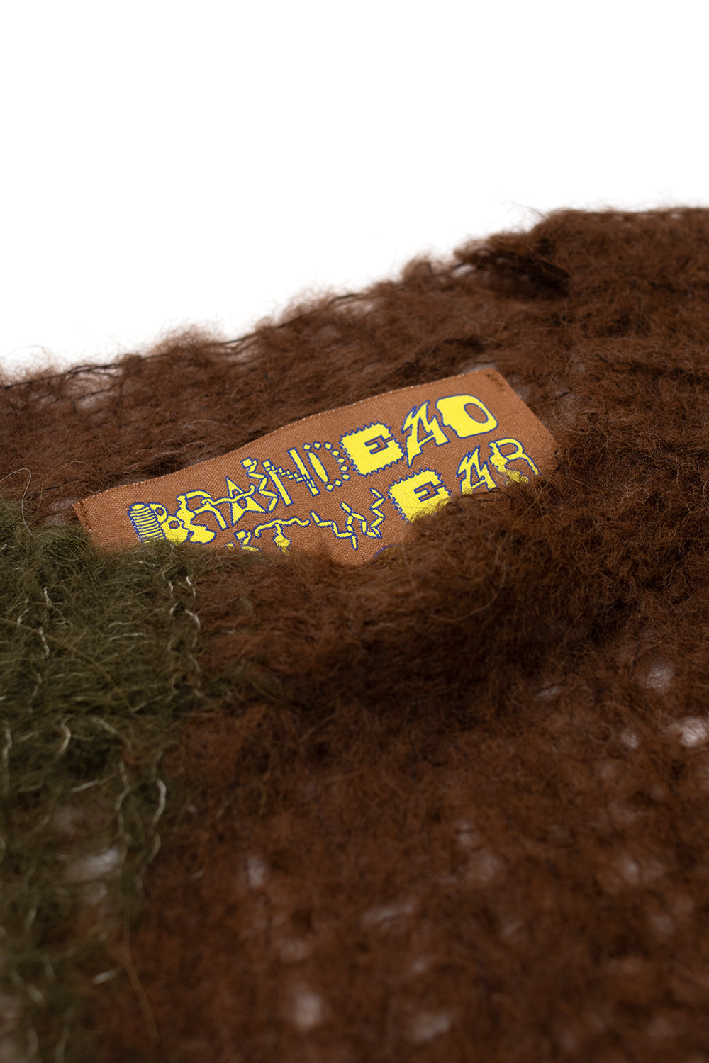 Close-up of Brain Dead Organic Threadbare Sweater Olive showing fuzzy alpaca yarn texture and Brain Dead knitwear label on lightweight organic threadbare sweater made in Peru
