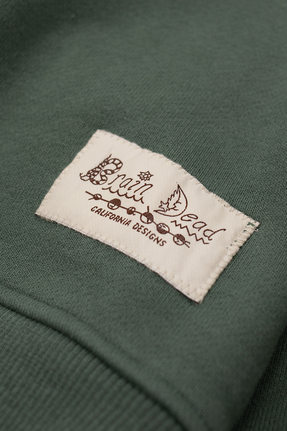 Brain Dead California Designs stitched logo patch on green Turtle Neck Sweatshirt highlighting branded label detail on premium cotton streetwear pullover made in Portugal