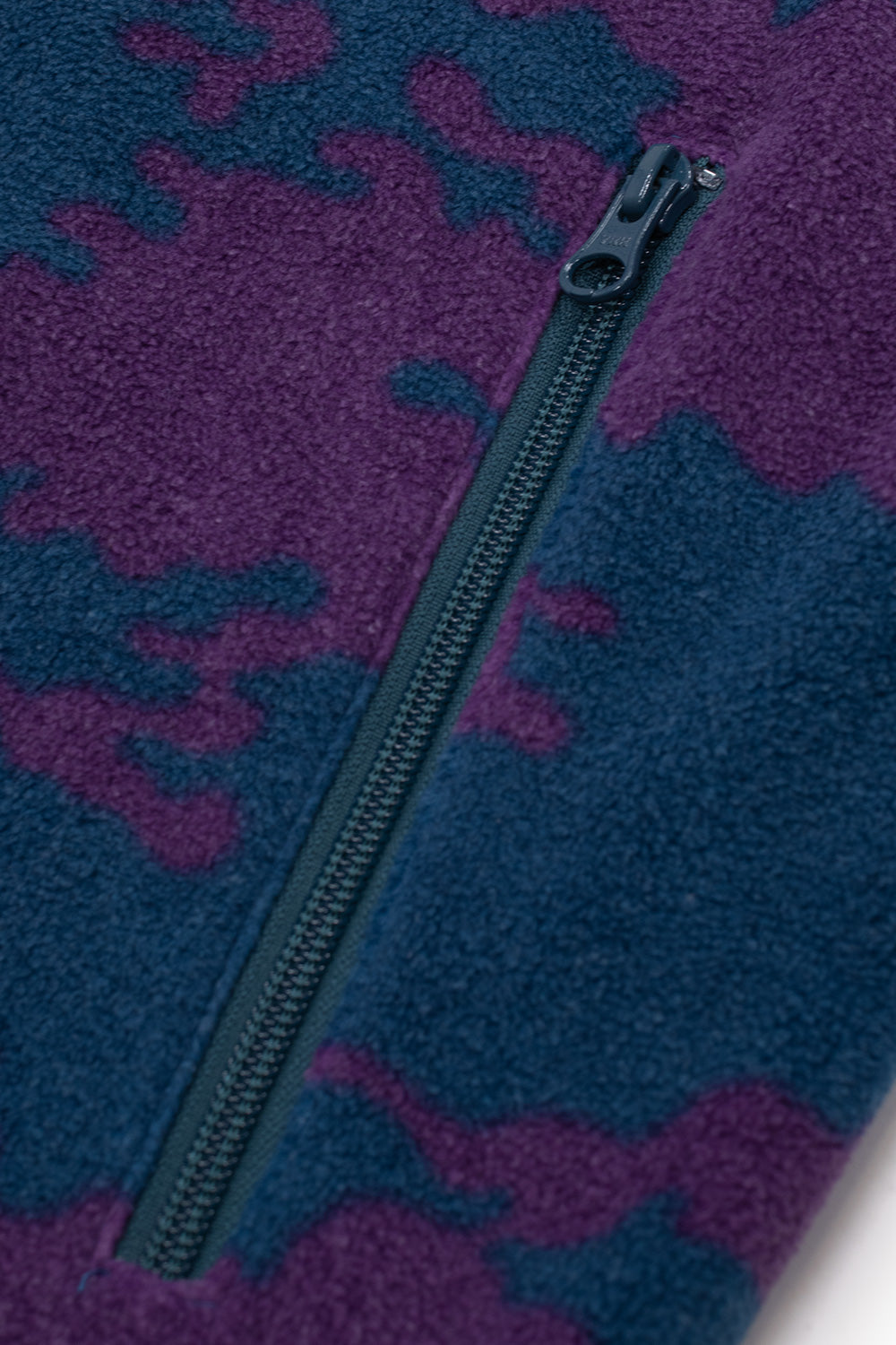 Macro detail shot of the side hand pocket on the By Parra Purple Darwin Camo Fleece, displaying the vertical blue YKK zipper with metal pull set into the soft two-tone abstract camouflage fleece fabric.