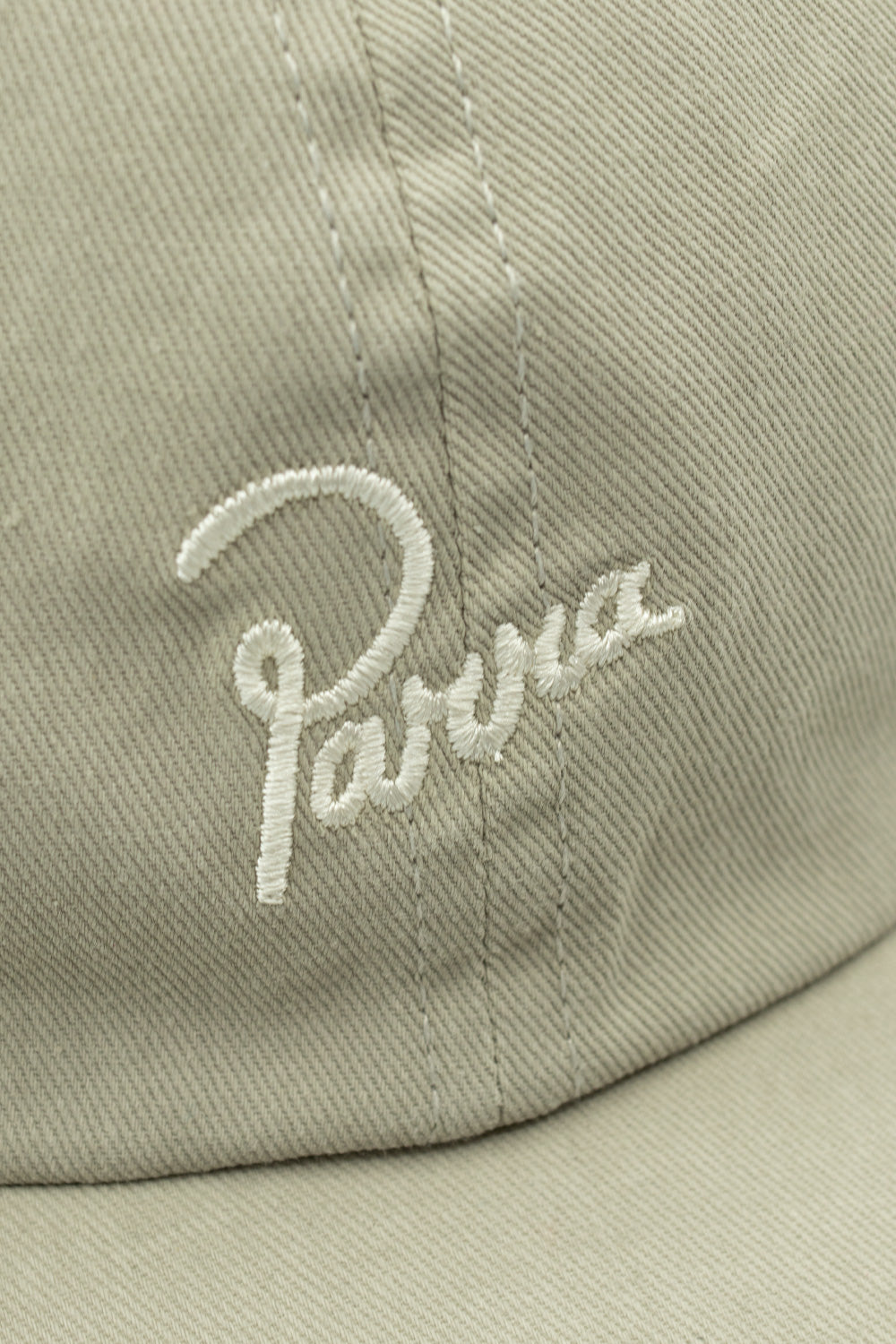 Extreme close-up macro detail of the off-white cursive Parra brand logo embroidery stitched on the washed grey cotton twill fabric of the cap crown.