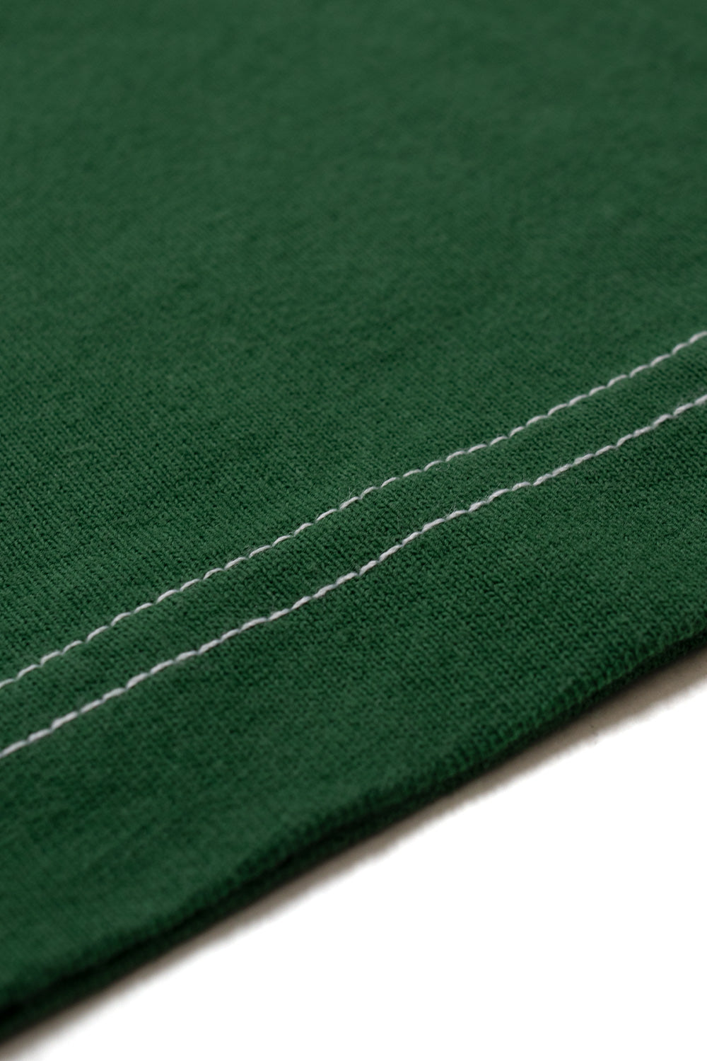 Detailed macro view of the sleeve cuff on the green By Parra Signature T-Shirt, showing the clean twin-needle white contrast stitching running parallel across the premium textured 240g cotton jersey hem.
