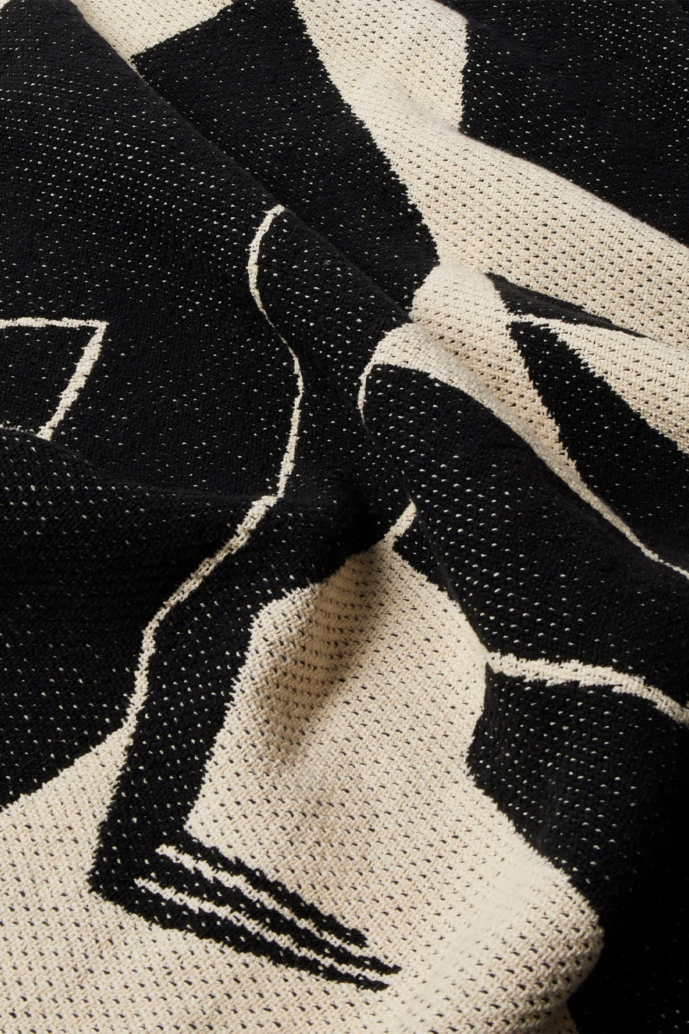 Macro close-up shot of the textured surface of the By Parra Waiting For You Throw Blanket, highlighting the detailed interwoven black and ecru cotton threads of the jacquard weave outlining the fluid abstract curves of the graphic art.