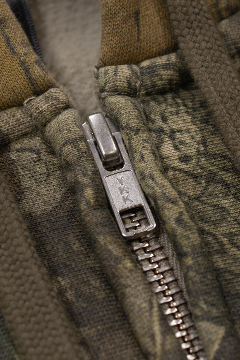 Detailed macro view of the premium metallic silver YKK two-way zipper mechanism on the heavy-weight Death Rites camouflage hoodie.