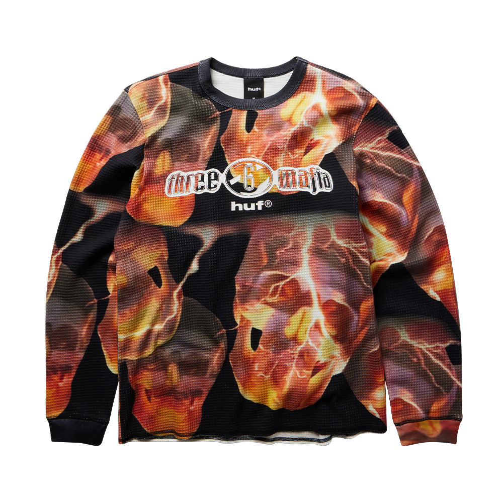 Front flat lay view of the Huf X Three 6 Mafia Torched Longsleeve Thermal shirt, made from textured waffle knit fabric covered in an allover photographic graphic of fiery burning skulls and lightning, featuring black ribbed cuffs and crewneck collar, and a center chest screen print of the metallic chrome Three 6 Mafia logo above a white lowercase "huf®" mark.