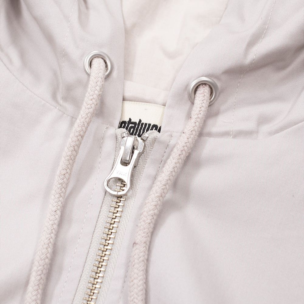 Macro studio close-up of the neckline and hood on the Metalwood Studio Cotton Twill Parka, detailing the silver metallic eyelets, thick braided cotton drawcords, brushed silver YKK zipper puller, and the woven cream "metalwood studio" neck label.
