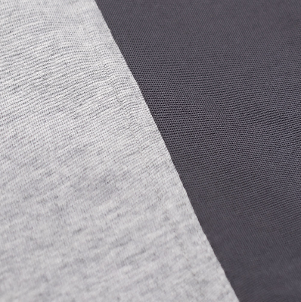 Extreme macro close-up of the ergonomic side panel on the Metalwood Studio Creature T-Shirt, detailing the precision overlock seam joining the textured, multi-tonal heather grey cotton knit to the smooth, solid charcoal grey side insert.