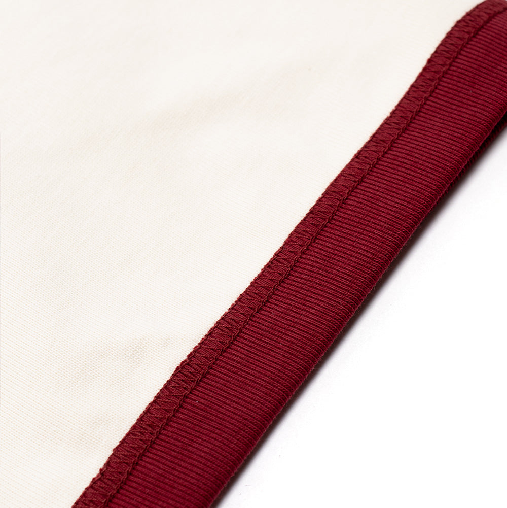 Extreme macro close-up of the sleeve cuff on the Metalwood Studio Dual Face T-Shirt, detailing the clean tonal flatlock seam connecting the fine-gauge burgundy ribbed cuff band to the soft, solid off-white cotton fabric.