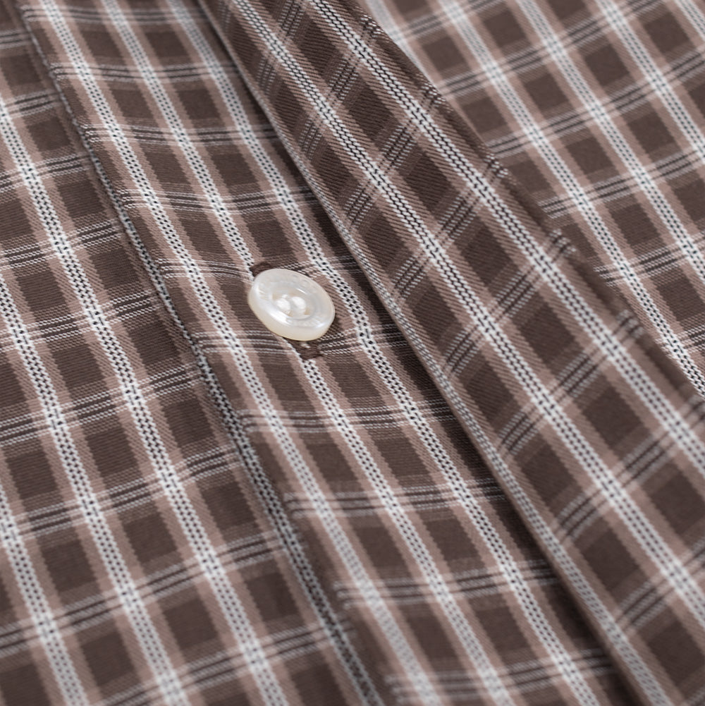 Close-up shot of the concealed button placket on the Metalwood Studio Frankenstein Shirt, folded open to reveal the hidden white mother-of-pearl style fastener stitched into the brown and white micro-plaid woven textile.