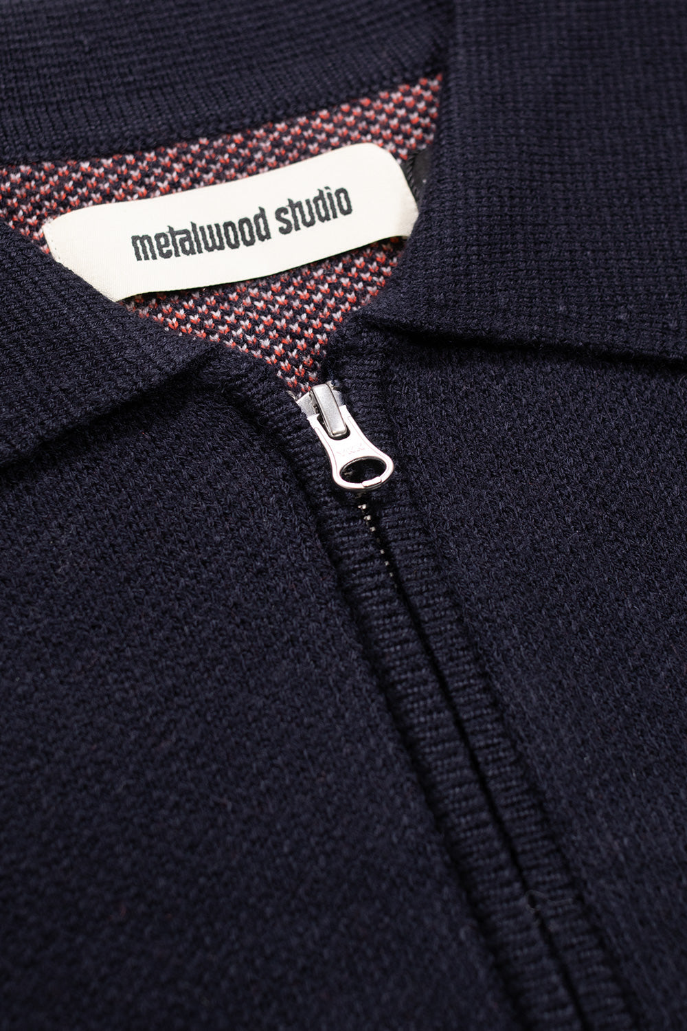 Close-up of the Metalwood Studio Kiki Zip Knit Polo collar and two-way YKK front zipper, highlighting the textured navy knit and interior contrast lining.