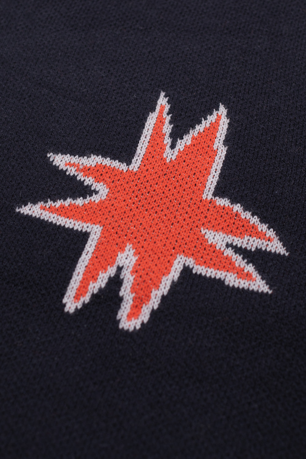 Detailed close-up of the woven red star graphic on the Metalwood Studio navy Kiki Zip Knit LS Polo, emphasizing the premium wool-blend knit texture.