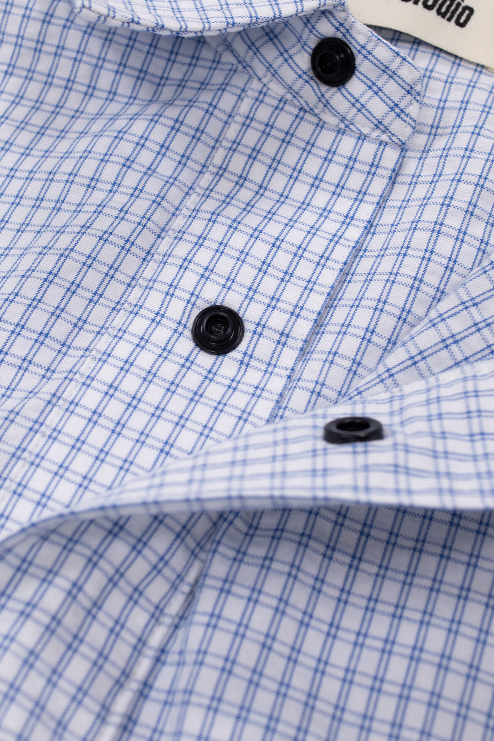 Close-up of front press-button closure on a white blue plaid cotton overshirt from Metalwood Studio with elevated workwear styling