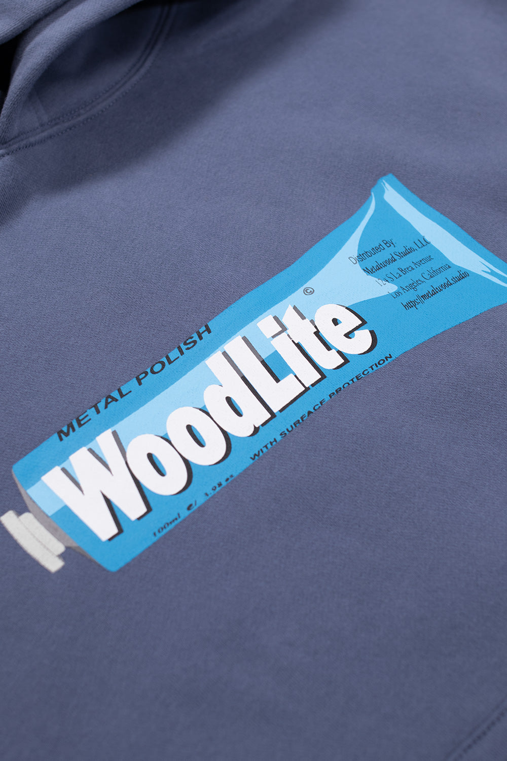 Close-up of the WoodLite metal polish graphic printed on the front of the Metalwood Studio steel hooded sweatshirt, highlighting vibrant blue artwork and premium print quality.