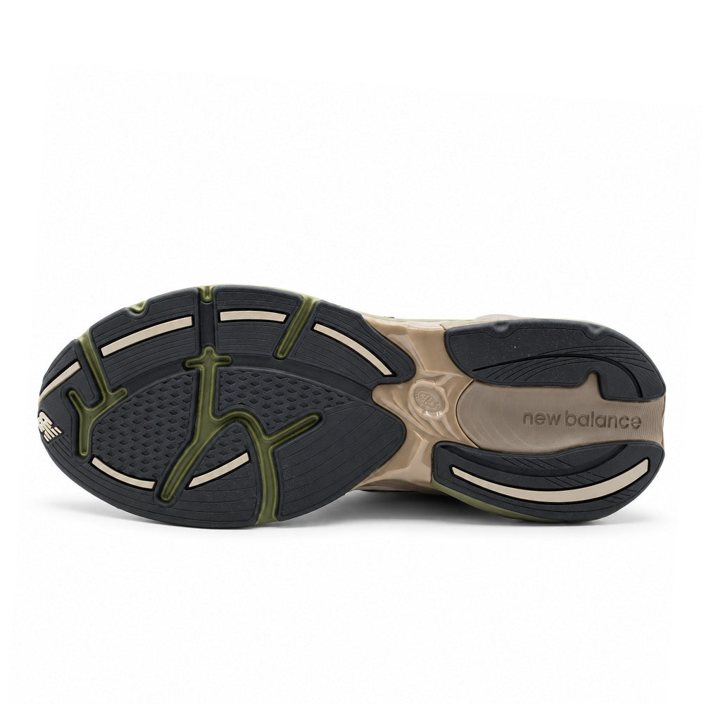Direct flat studio view of the treaded rubber outsole on the New Balance 2010 (GORE-TEX), detailing the segmented multidirectional traction pattern in black and beige rubber, olive green stability web support shank, and molded "new balance" arch branding.