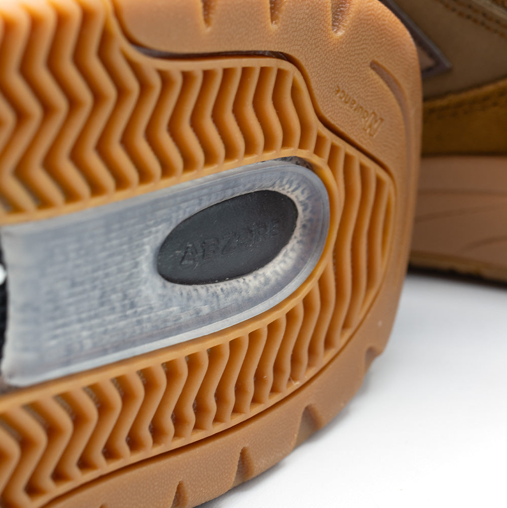 Extreme macro close-up of the heel outsole tread on the New Balance Numeric Andrew Reynolds 933, detailing the grooved gum Ndurance rubber herringbone traction pattern and the clear central window exposing the black shock-absorbing ABZORB heel cushioning pod.