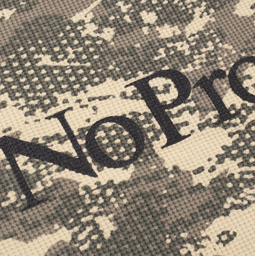 Detailed macro studio close-up of the chest graphic on the Aries No Problemo Forest Waffle Long Sleeve Shirt, capturing the grid-like thermal knit fabric structure, sand and olive digital dot-matrix camouflage pattern, and the crisp matte black screen-printed serif typography of the "No Problemo" branding.