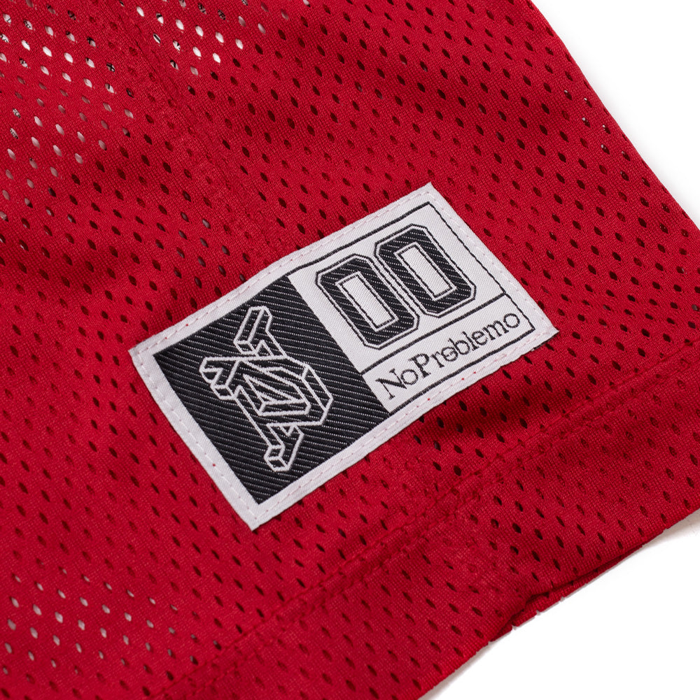 Macro studio view of the lower hem branding on the red Aries No Problemo NYP Sports Mesh Jersey, highlighting the retro white woven athletic locker jock tag featuring black geometric Aries temple graphics, varsity number "00", and serif "No Problemo" typography.