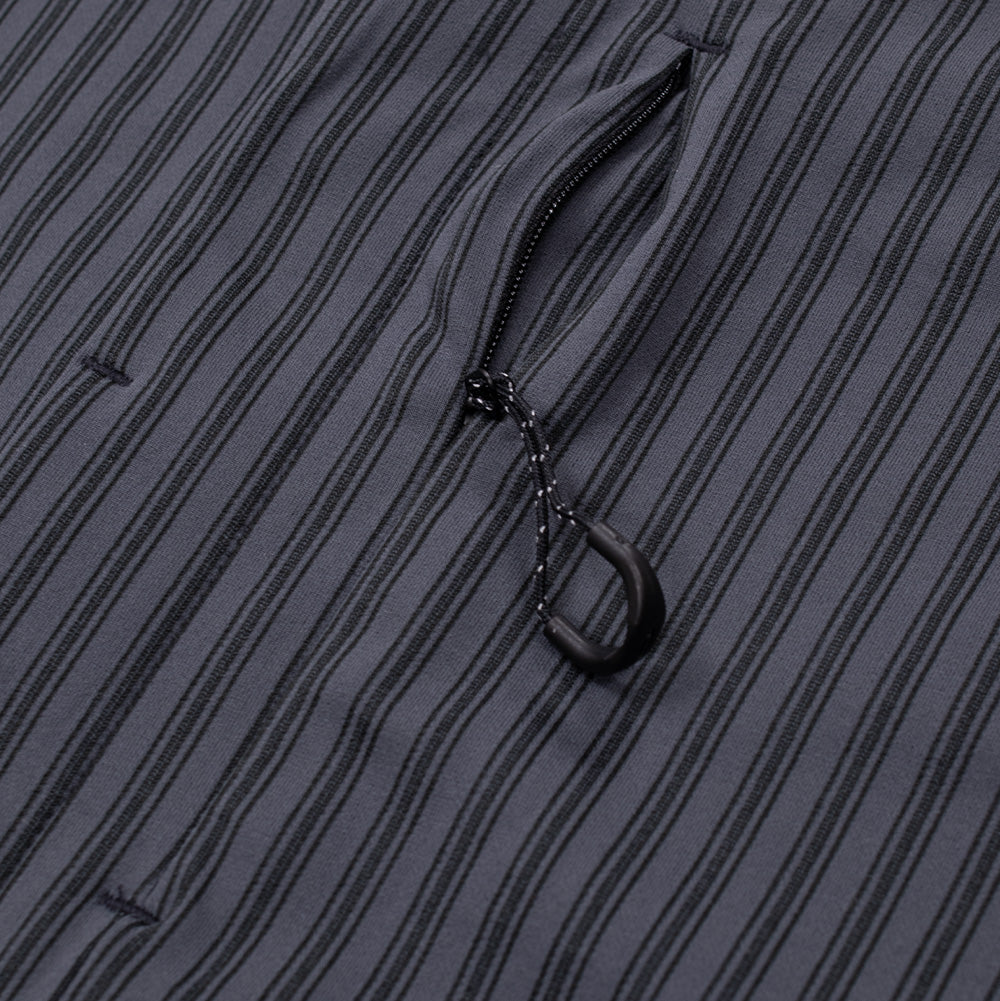 Detailed macro perspective of the vertical chest pocket on the Oakley FGL Fuel Shirt, highlighting the narrow concealed zipper track set into the dark grey striped technical textile, equipped with a black textured loop cord puller.