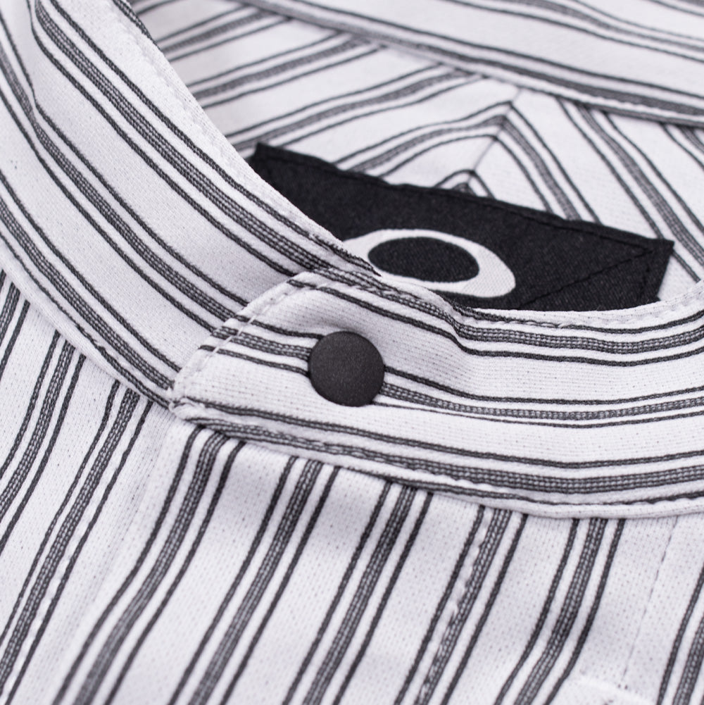 Macro studio close-up of the mandarin band collar and neckline on the Oakley FGL Fuel LS Shirt, showing the horizontal stripe pattern along the collar band, matte black top snap button, woven black Oakley brand label, and chevron interior back yoke alignment.