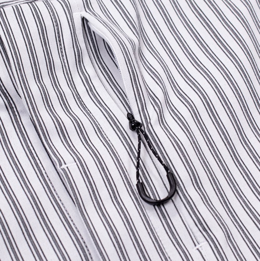 Detailed macro perspective of the vertical chest pocket on the white Oakley FGL Fuel Shirt, highlighting the narrow reverse-coil zipper track integrated into the striped technical textile, completed with a black paracord pull loop with textured rubber grip.