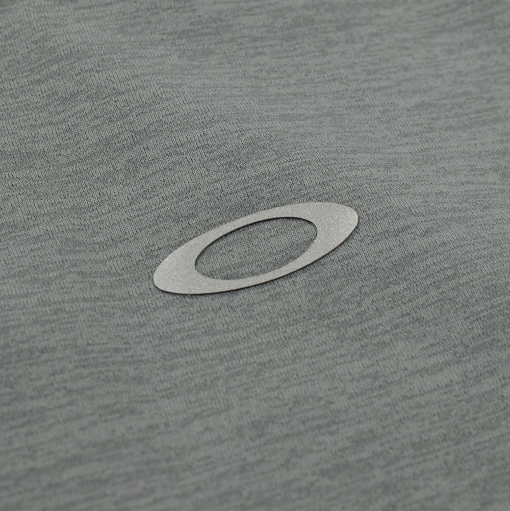 Extreme macro close-up of the upper back branding on the Oakley FGL Scratch SS Tee, featuring the reflective metallic silver heat-transfer Oakley Ellipse emblem cleanly bonded onto the soft heathered green performance knit fabric.