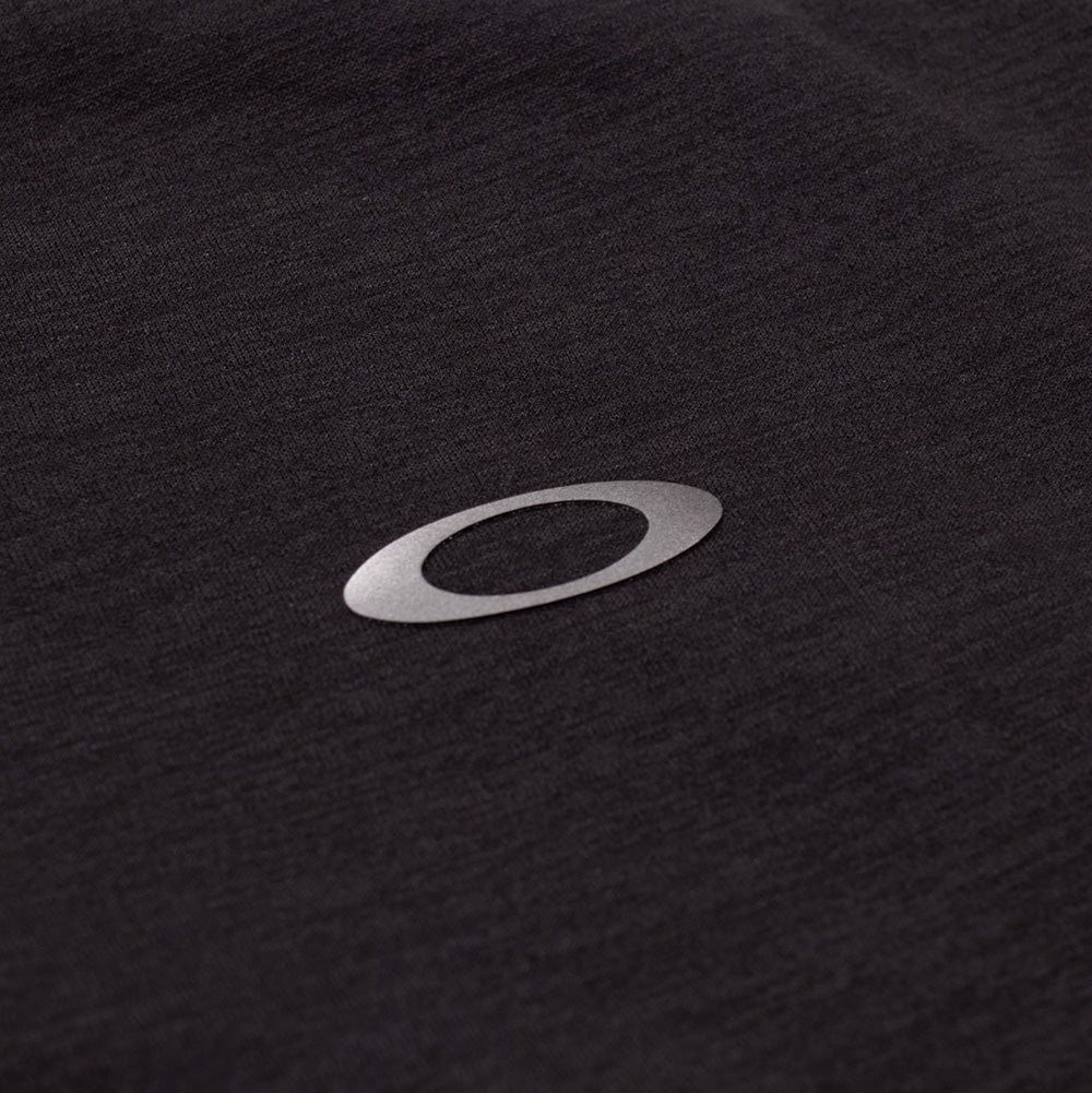 Extreme macro close-up of the rear collar branding on the Oakley FGL Scratch SS Tee, focusing on the metallic silver reflective heat-transfer Oakley Ellipse emblem bonded securely onto the smooth, moisture-wicking charcoal jersey fabric.