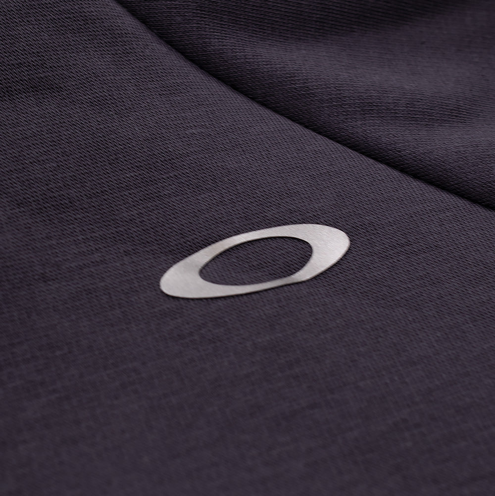 Extreme macro close-up of the rear shoulder branding on the Oakley FGL Slick Fleece Hoodie, showcasing the reflective metallic silver heat-transfer Oakley Ellipse logo seamlessly applied to the dense, smooth-faced dark charcoal technical fleece material.
